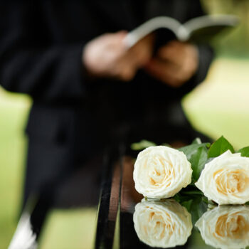 Closeup of two white roses on coffin at outdoor funeral ceremony, copy space
